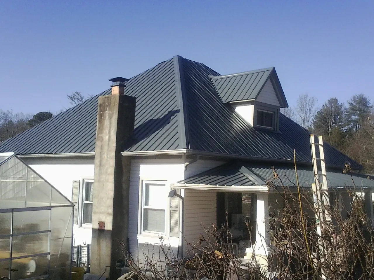Dark blue standing seam metal roof on a white farmhouse with dormer — Slate & Tile Roof Repair by Roofing Brothers in Encampment