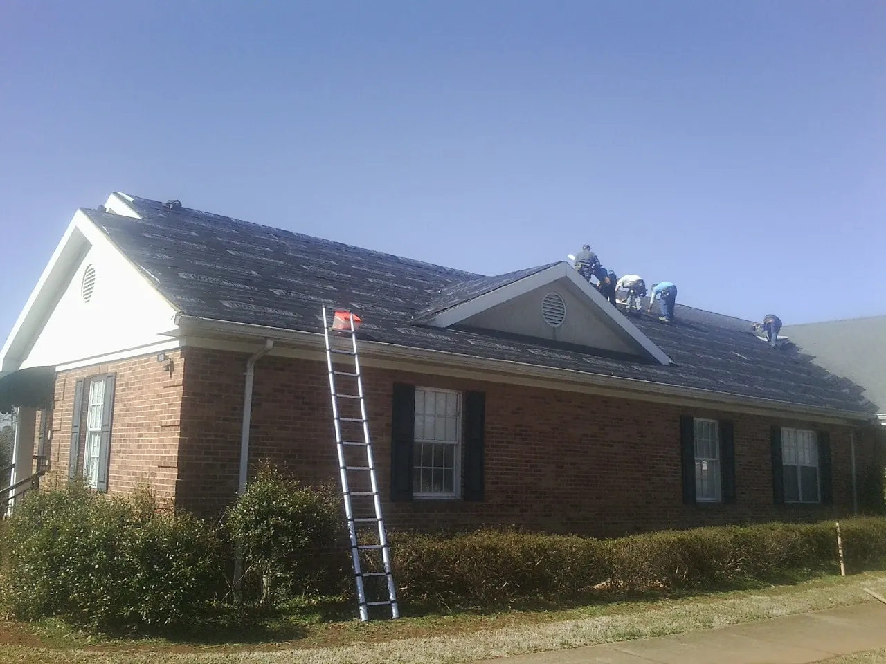 Crew tearing shingles off a brick ranch roof with a ladder set — Emergency Roof Repair work by our crew in Encampment