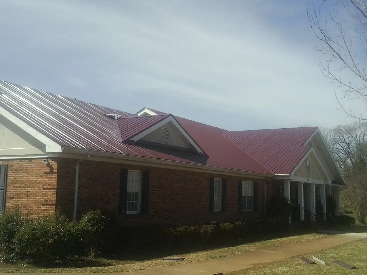 Red metal roof with gabled entries on a long brick building, from a Hail Damage Roof Repair job in Encampment