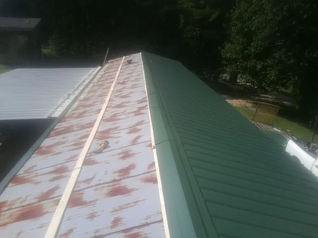 Old rusted panels beside newly installed green metal roofing — Wind Damage Roof Repair by Roofing Brothers in Encampment