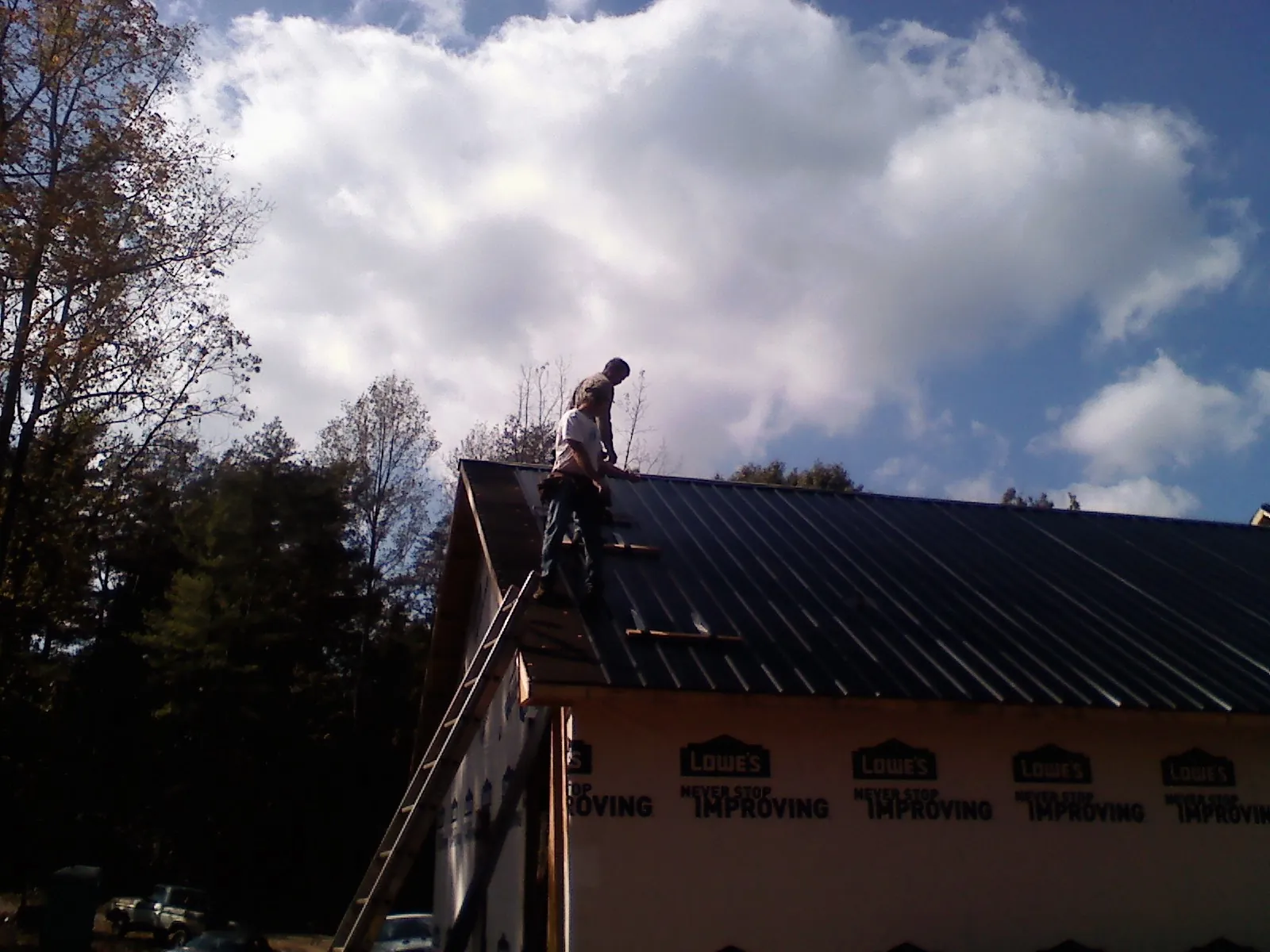 Roofer fastening dark metal panels high against a cloudy sky, from a Roof Inspection job in Encampment