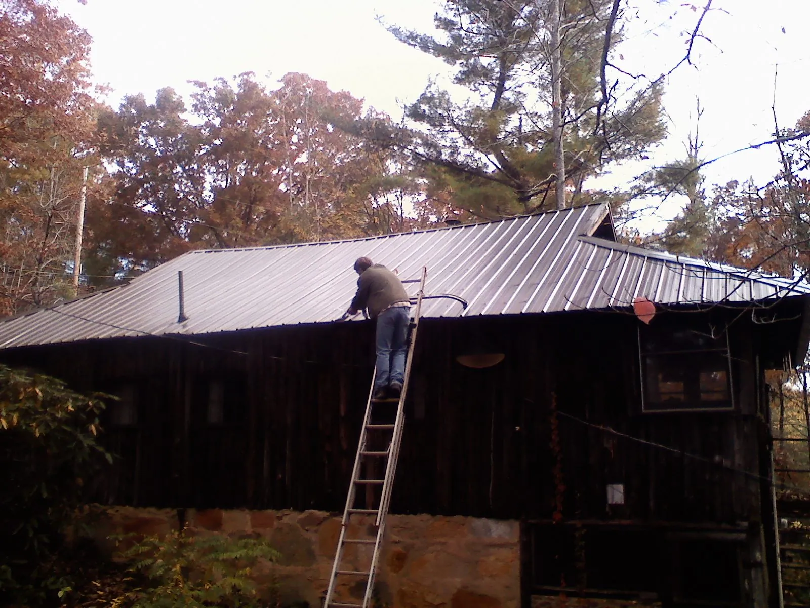 Roofer on a ladder working along the edge of a cabin metal roof in Encampment