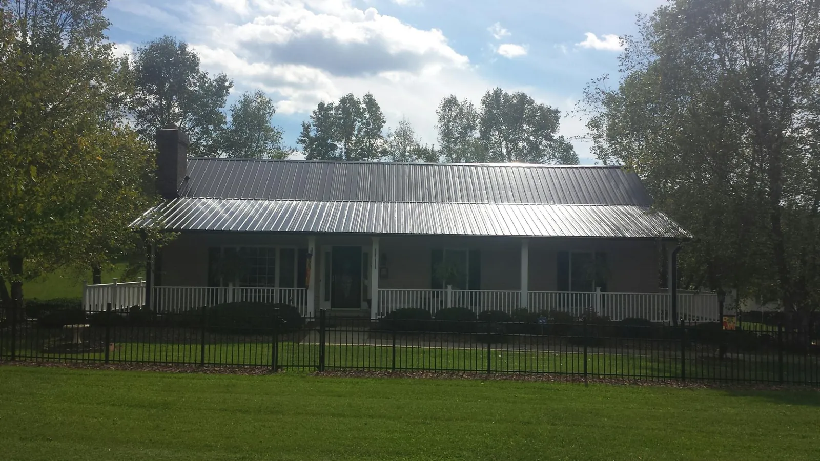 Gray metal roof on a brick ranch with a full width front porch — Gutter Guard Installation work by our crew in Encampment