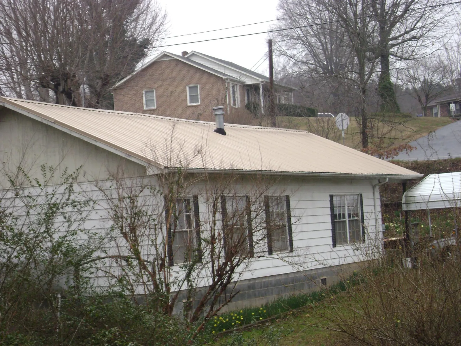 Tan metal roof on a white sided house set into a hillside — Commercial Roofing by Roofing Brothers in Encampment